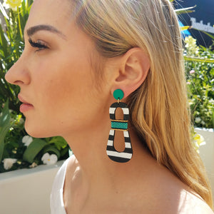 Model with blond hair wearing modern, curvy, black and white striped statement earrings with hand-beaded teal accents by the brand SCOTCHBONNET.