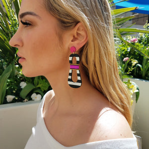 Blond model wearing modern, curvy, black and white striped statement earrings with hand-beaded magenta accents by the brand SCOTCHBONNET.