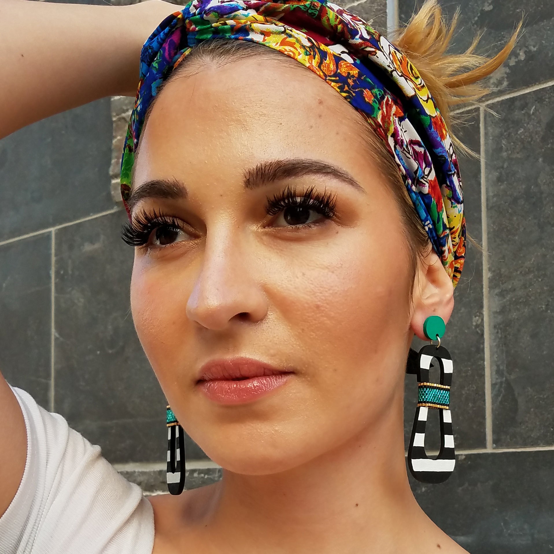 Model with colorful headband wearing modern, curvy, black and white striped statement earrings with hand-beaded teal accents by the brand SCOTCHBONNET.