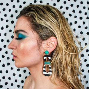 Model with teal eyeshadow wearing modern, curvy, black and white striped statement earrings with hand-beaded teal accents by the brand SCOTCHBONNET.
