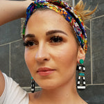Model with colorful headband wearing modern, curvy, black and white striped statement earrings with hand-beaded teal accents by the brand SCOTCHBONNET.