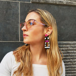 Model with magenta sunglasses wearing modern, curvy, black and white striped statement earrings with hand-beaded magenta accents by the brand SCOTCHBONNET.