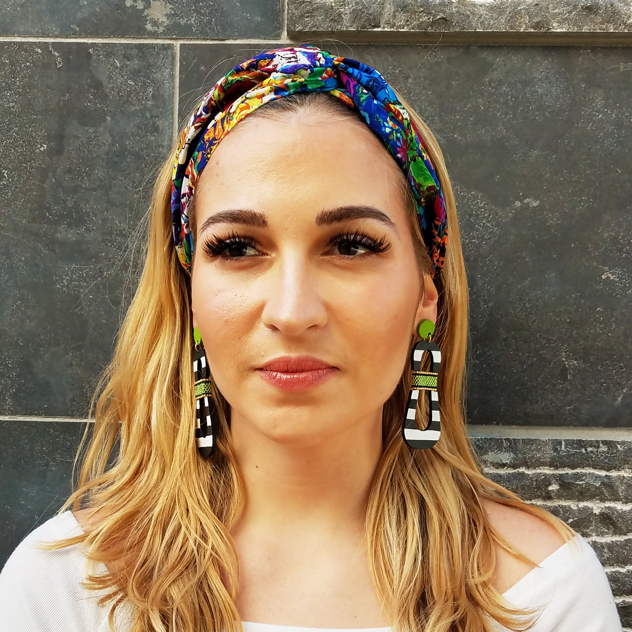 Model with colorful headband wearing modern, curvy, black and white striped statement earrings with hand-beaded chartreuse accents by the brand SCOTCHBONNET.