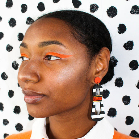 Model with orange eyeshadow wearing modern, curvy, black and white striped statement earrings with hand-beaded orange accents by the brand SCOTCHBONNET.