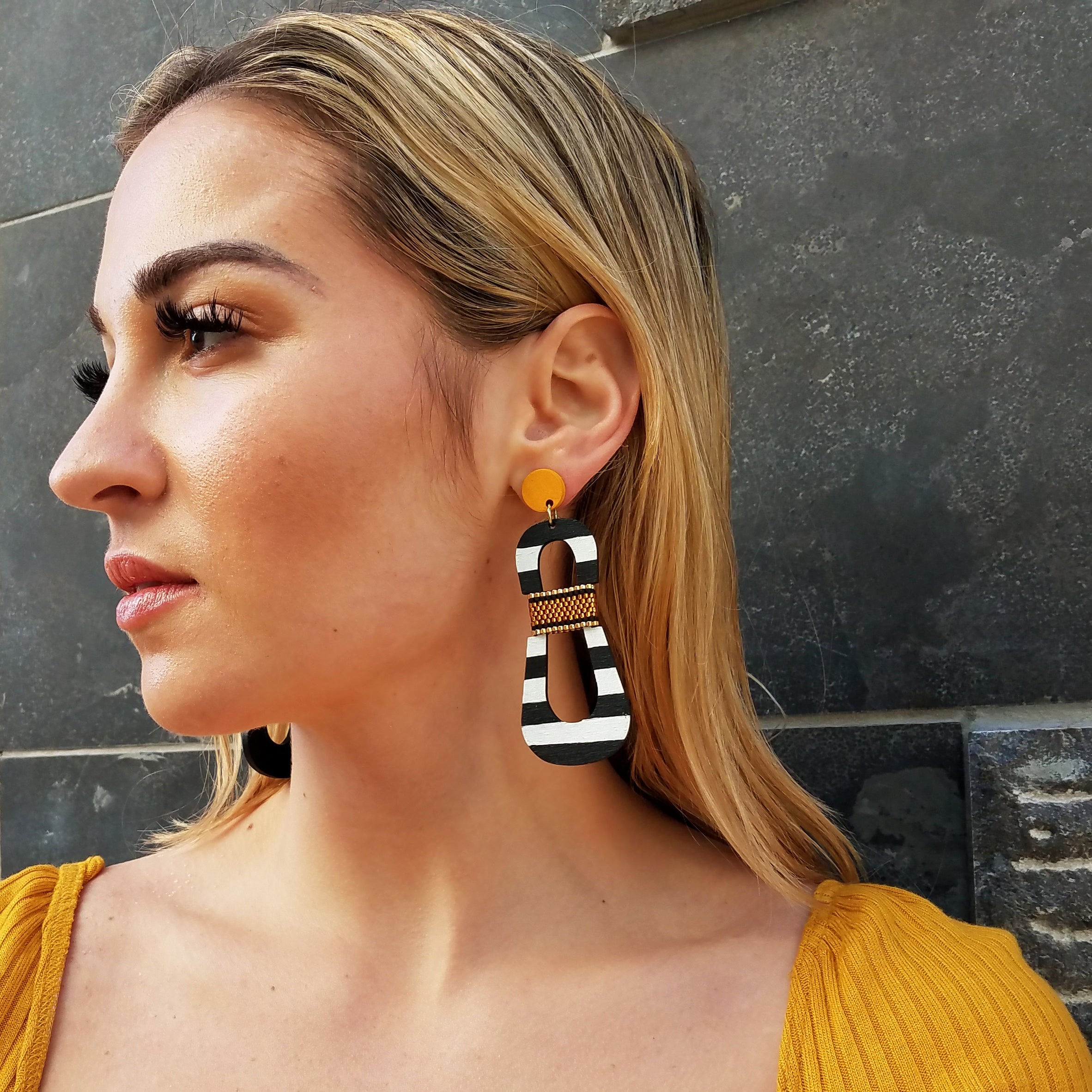 Side view of model wearing modern, curvy, black and white striped statement earrings with hand-beaded yellow accents by the brand SCOTCHBONNET.