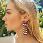 Model with blonde hair wearing modern, curvy, black and white striped statement earrings with hand-beaded purple accents by the brand SCOTCHBONNET.