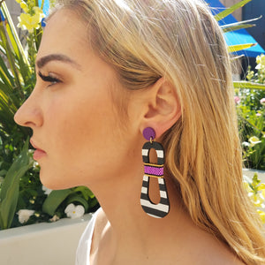 Model with blonde hair wearing modern, curvy, black and white striped statement earrings with hand-beaded purple accents by the brand SCOTCHBONNET.