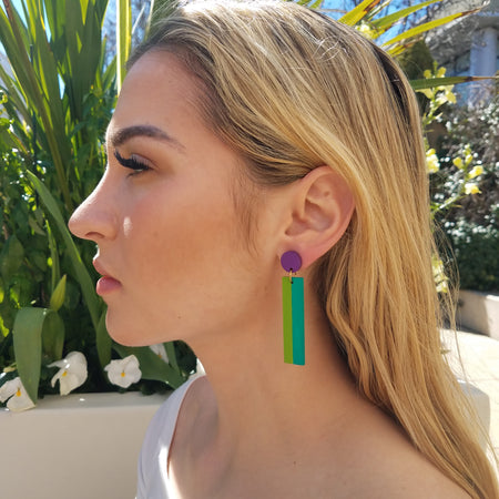 Model with blonde hair wearing geometric color blocked statement earrings in bright shades of purple, green and teal by the brand SCOTCHBONNET.