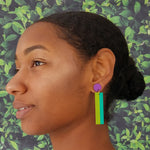 Model with dark hair wearing geometric color blocked statement earrings in bright shades of purple, green and teal by the brand SCOTCHBONNET.