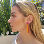 Model with blonde hair wearing geometric color blocked statement earrings in bright shades of magenta, orange and yellow by the brand SCOTCHBONNET.