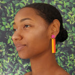 Model with dark hair wearing geometric color blocked statement earrings in bright shades of magenta, orange and yellow by the brand SCOTCHBONNET.