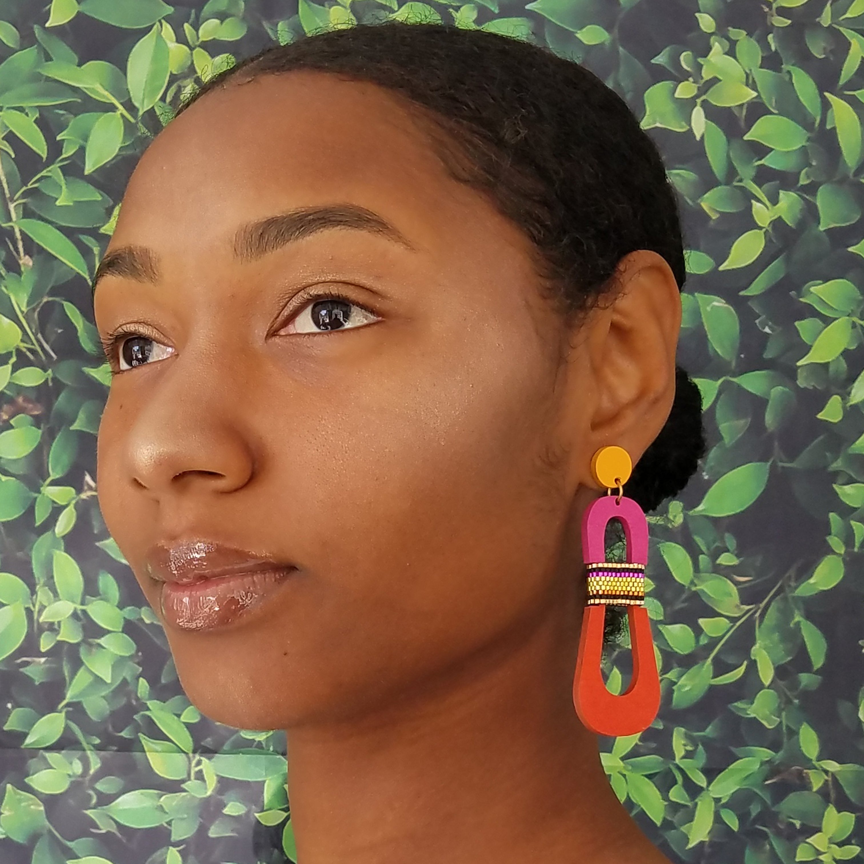 Model with dark hair wearing modern, curvy, yellow, magenta and orange color blocked statement earrings with hand-beaded accents by the brand SCOTCHBONNET.