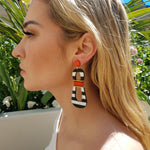 Model with blonde hair wearing modern, curvy, black and white striped statement earrings with hand-beaded orange accents by the brand SCOTCHBONNET.