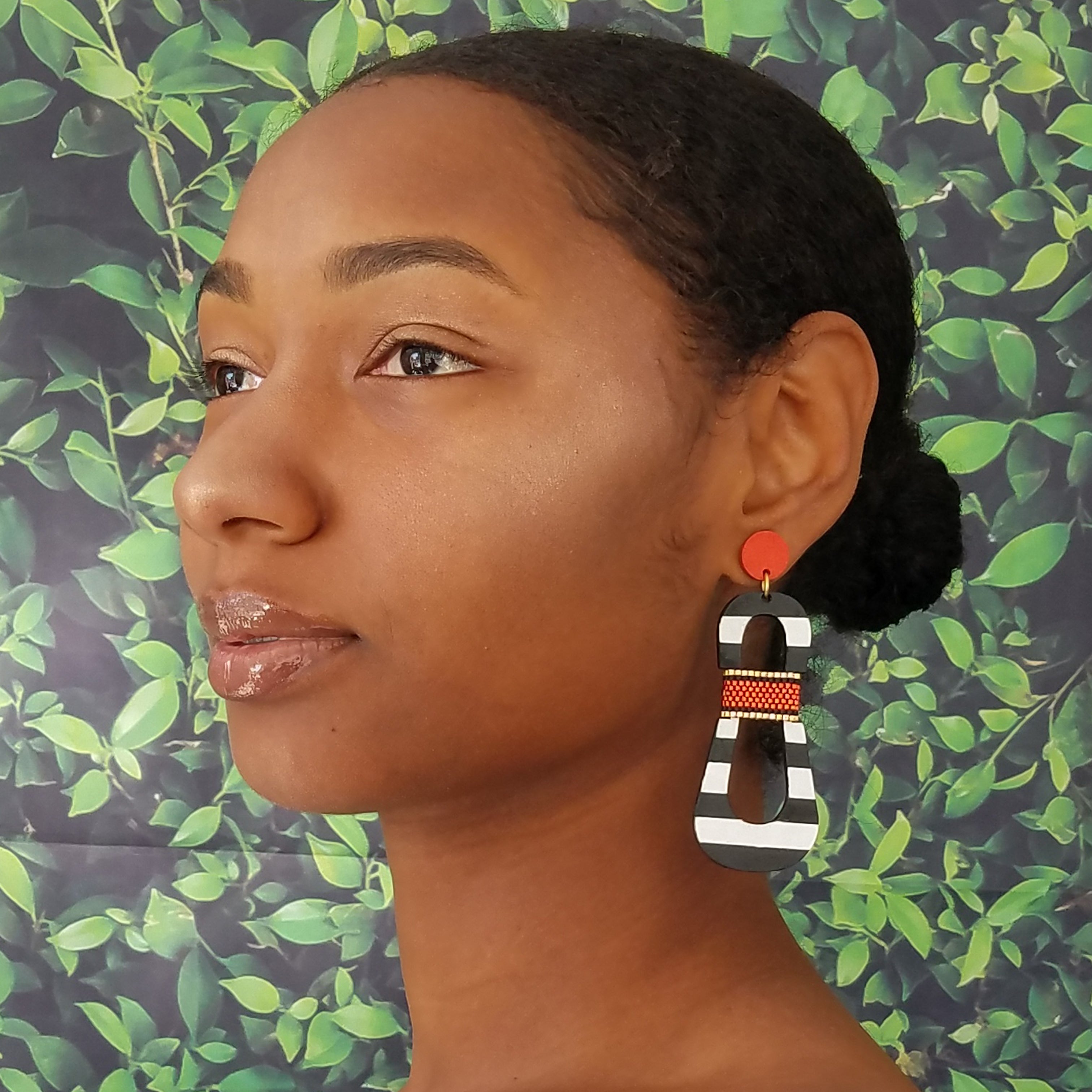 Model with dark hair wearing modern, curvy, black and white striped statement earrings with hand-beaded orange accents by the brand SCOTCHBONNET.
